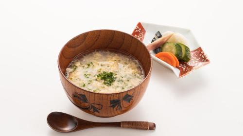 a soup in a wooden bowl on a table with a spoon at Hotel Sumire ふぐ料理を愉しむ料理宿 in Shimonoseki