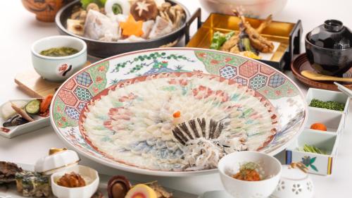 a large plate of food on a table with other dishes at Hotel Sumire ふぐ料理を愉しむ料理宿 in Shimonoseki