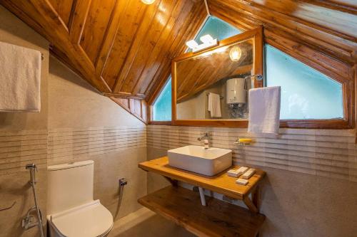 a bathroom with a sink and a toilet and a window at Nau Nabh Cottage by VEO - Part of StayVista in Shimla