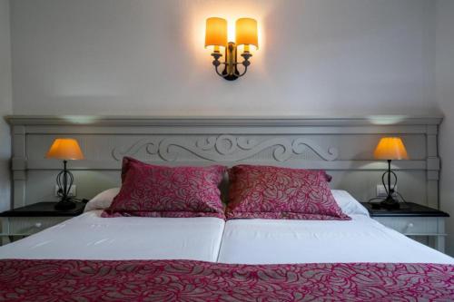 a bedroom with a white bed with pink pillows and two lamps at Club Cala Domingos in Calas de Mallorca