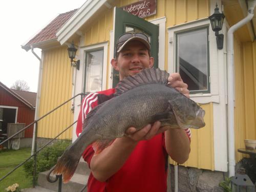 a man holding a fish in front of a house at Älgbergets Bed & Breakfast in Ucklum