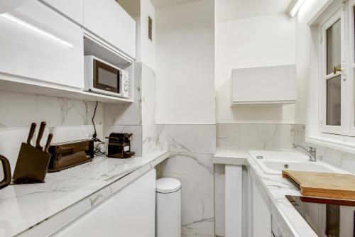 - une cuisine blanche avec des comptoirs en marbre et un évier dans l'établissement Best Location Calm Palais Royal Louvre Opera Concorde CLIM, à Paris