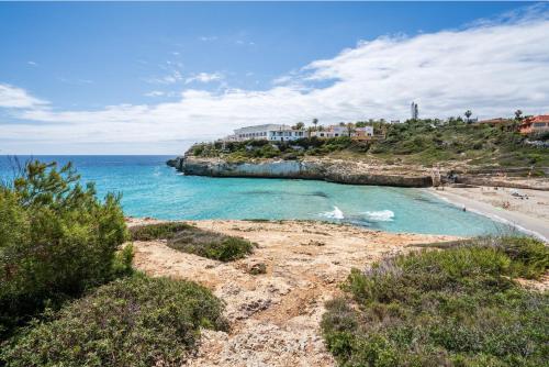 a beach with a house on a hill next to the ocean at Club Cala Domingos in Calas de Mallorca