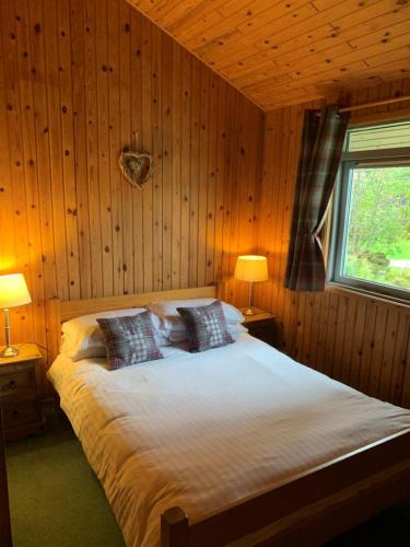 a bedroom with a bed with two lamps and a window at Milton Bay Luxury lodge wrapped in exceptional scenery in Morenish
