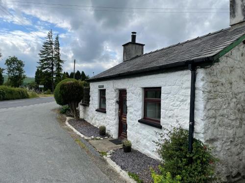 a white building with a window on the side of a road at Bimble cottage. The Cosy Snowdonia Hideaway in Llanuwchllyn