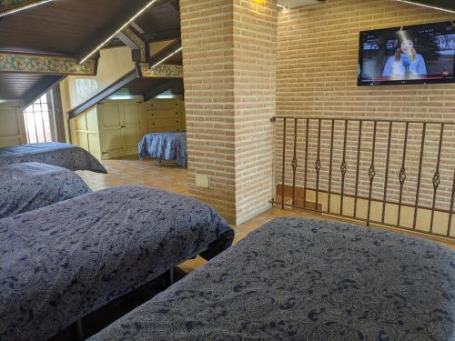 Habitación con 3 camas y TV en una pared de ladrillo. en Villa El Rosal del Pozo, en Layos