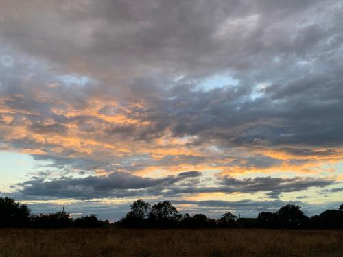 a cloudy sky over a field with trees in the background at Bluebell Barn in Banham
