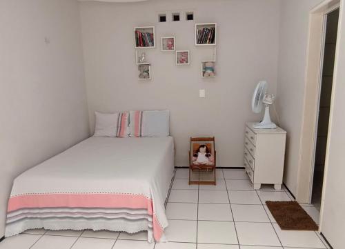 a white bedroom with a bed and a small cabinet at Sua casa fora de casa in Fortaleza