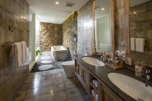 a bathroom with two sinks and a toilet and a tub at The Sun of Granary Resort and Villas in Ubud