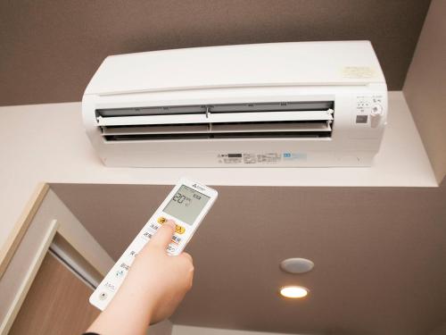 a person holding a remote control in front of a air conditioner at Hotel Route-Inn Saku Minami Inter in Saku