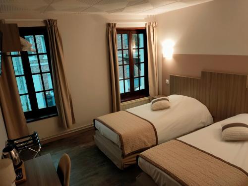 a bedroom with two beds and a table and windows at Au Lion d'or in Saint-Pol-sur-Ternoise