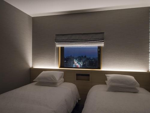 two beds in a hotel room with a window at Tmark City Hotel Kanazawa in Kanazawa