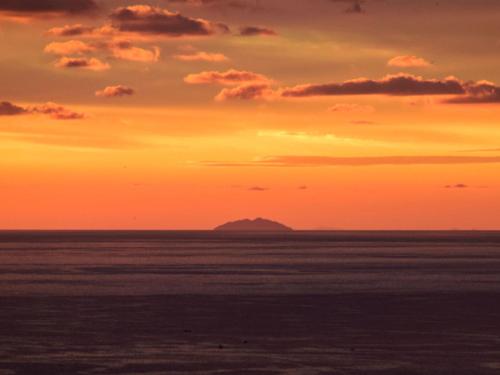 a sunset over the ocean with a mountain in the distance at Hanareya in Tsushima