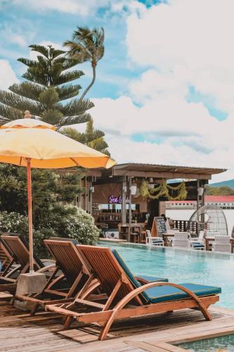 a group of chairs and an umbrella next to a swimming pool at Tango Luxe Beach Villa, Koh Samui in Choeng Mon Beach