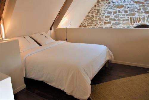 una camera con un letto bianco e un muro in pietra di Maison de contes en amoureux a Taden