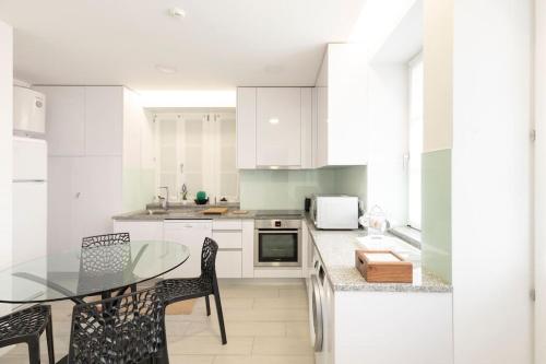 a kitchen with white cabinets and a glass table and chairs at Apartamento Avenida in Viana do Castelo