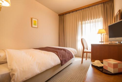 a hotel room with a bed and a desk with a television at Hotel Wakamizu in Takarazuka