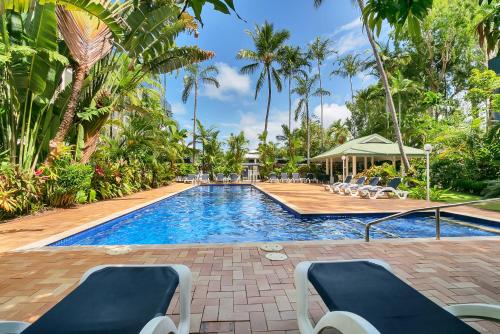 a swimming pool with lounge chairs and palm trees at Agincourt Beachfront Apartments in Clifton Beach