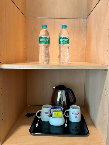 a tea kettle and cups on a shelf with water bottles at Sendale Tainan Science Park Hotel in Xinshi