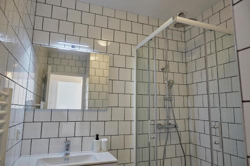 La salle de bains est pourvue de carrelage blanc, d'un lavabo et d'un miroir. dans l'établissement Appartement front mer proche omaha & utah beach - 2, à Grandcamp-Maisy