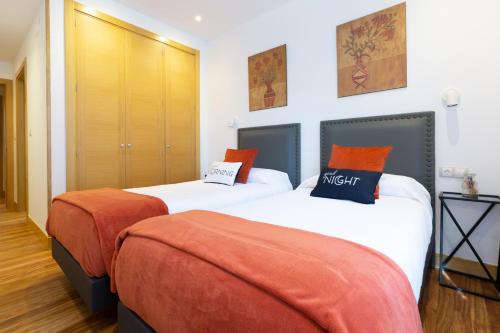 2 Betten mit orangefarbenen Kissen in einem Zimmer in der Unterkunft Unamuno by Bilbao Living in Bilbao