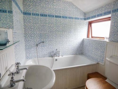 a blue tiled bathroom with a tub and a sink at Corner Cottage in Reynoldston