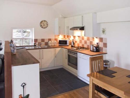 a kitchen with white cabinets and a clock on the wall at Curlew Cottage in Warslow