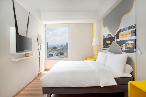 a bedroom with a white bed and a large window at KIMAYA Braga Bandung by HARRIS in Bandung