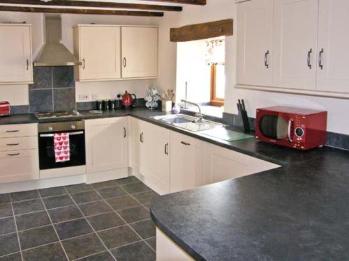 a kitchen with white cabinets and a red microwave at Stabal-y-Gwedd in Llanddulas