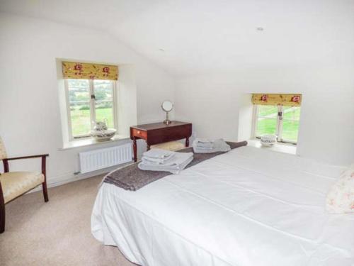 a white bedroom with a bed and a table and two windows at Rose Cottage in Monmouth