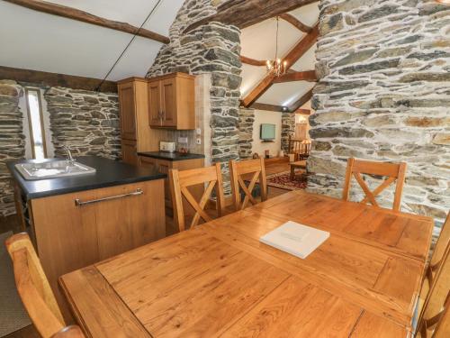 a kitchen with a wooden table and a stone wall at Hendoll Barn in Fairbourne
