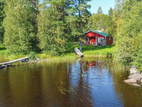 a red cabin by a lake with a boat in front at Holiday Home Saniainen 5 by Interhome in Säviä