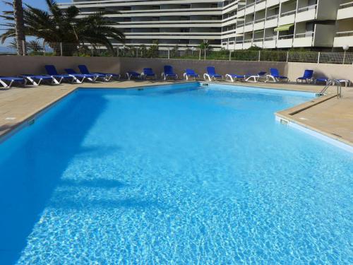 una grande piscina con sedie blu in un edificio di Apartment Copacabana-21 by Interhome a Canet-en-Roussillon