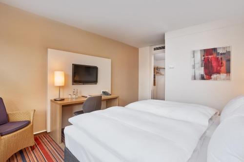 a hotel room with two beds and a desk and a tv at H+ Hotel Bochum in Bochum