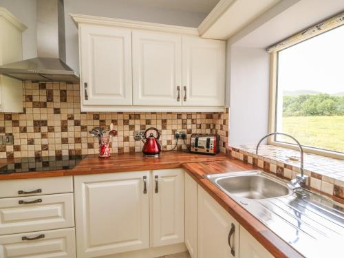 a kitchen with white cabinets and a sink and a window at Dromstabla in Glencar