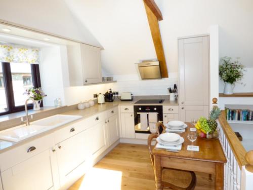 een keuken met witte kasten, een tafel en een wastafel bij Brightley Mill Barn in Okehampton