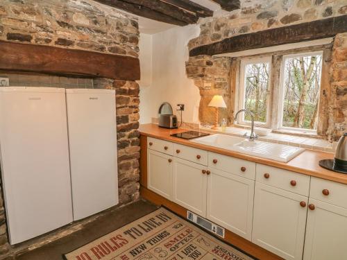 a kitchen with white cabinets and a sink and a window at Beckside Cottage in Mansergh