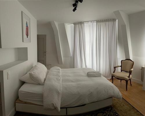 a white bedroom with a bed and a chair at Duplex dernier étage avec terasse à deux pas de la grand place in Brussels