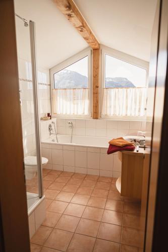 a bathroom with a tub and a toilet and two windows at Vitalpark Blaichach Burgberg in Burgberg