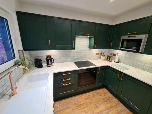 una cocina verde con armarios verdes y fregadero en The Editor's Choice, Oban seafront apartment en Oban