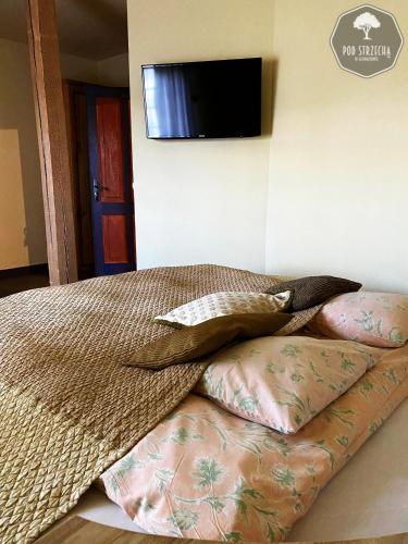 a bed with pillows and a television on a wall at Dom Wypoczynkowy "Pod Strzechą" w Giewartowie in Giewartów