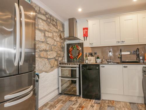 a kitchen with white cabinets and a stone wall at Chapel Green Studio 2 in St Austell