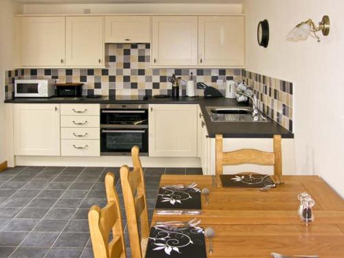 a kitchen with white cabinets and a wooden table with chairs at Ty Isaf Penrhyddion in Betws-y-coed