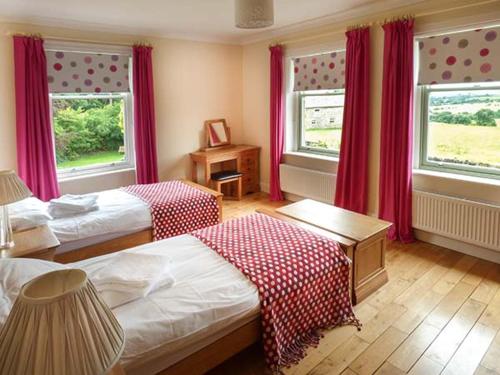 a bedroom with two beds and two windows with red curtains at Cringles House in Silsden