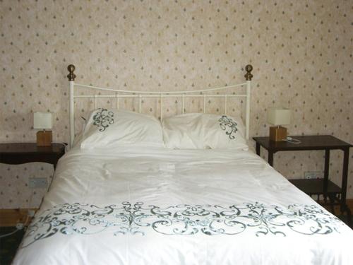 a bedroom with a white bed with two tables at Homestone Farm in Drumlemble