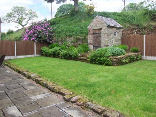um jardim com um edifício de pedra e um quintal com uma cerca em Horse Shoe Cottage em Bradley in the Moors
