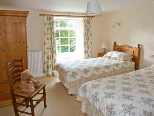 a bedroom with two beds and a teddy bear on a chair at High Kiln Bank Cottage in Ulpha