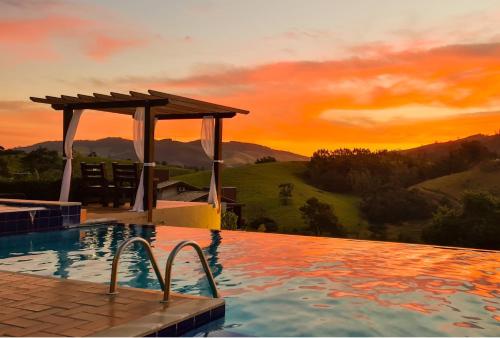 a swimming pool with a sunset in the background at Pousada Estância das Montanhas in Águas de Lindóia
