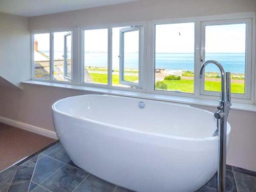 a large white tub in a bathroom with windows at Sea View Apartment in Llanfairfechan