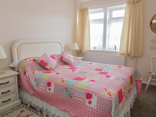 a bedroom with a pink and white bed with a window at Spurling Cottage in Cheveley